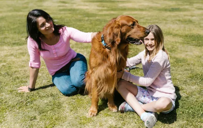 A girl and her mom sitting in the yard petting a dog